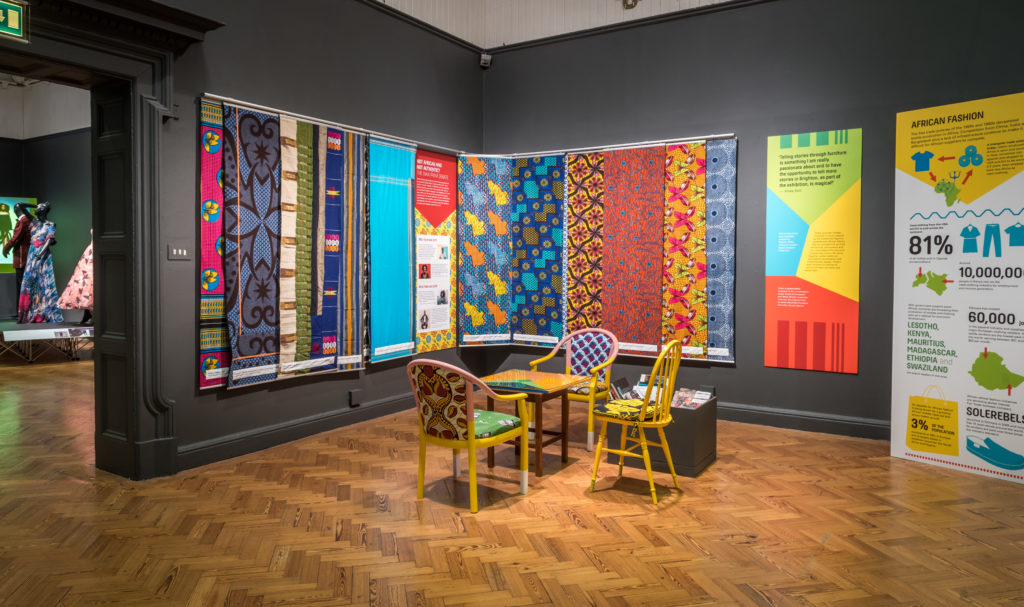 A museum gallery with dutch wax print panels on the walls, and colourful chairs upholstered in wax print