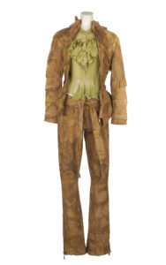 A mannequin wearing a brown leather camouflage print bomber jacket and matching trousers, with a pale green frilly blouse
