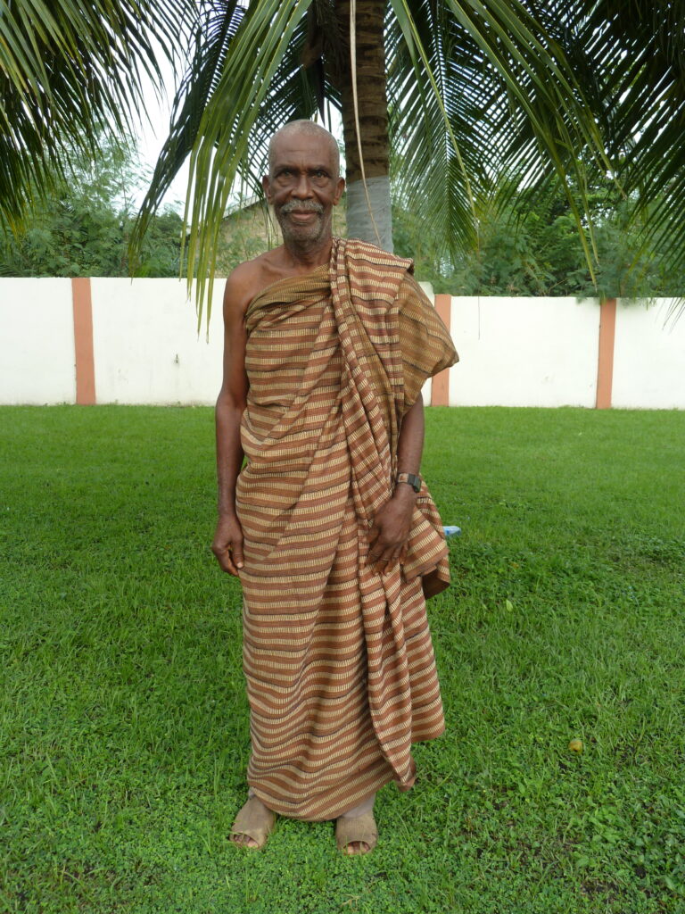 an older man wearing a kente standing in a garden