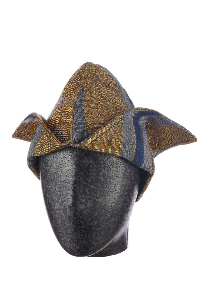 a man's blue and gold aso-oke cap with two triangular flaps on a mannequin head