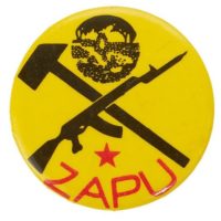 Round yellow pin badge reading 'ZAPU' in red letters, underneath a gun crossed with a hammer.