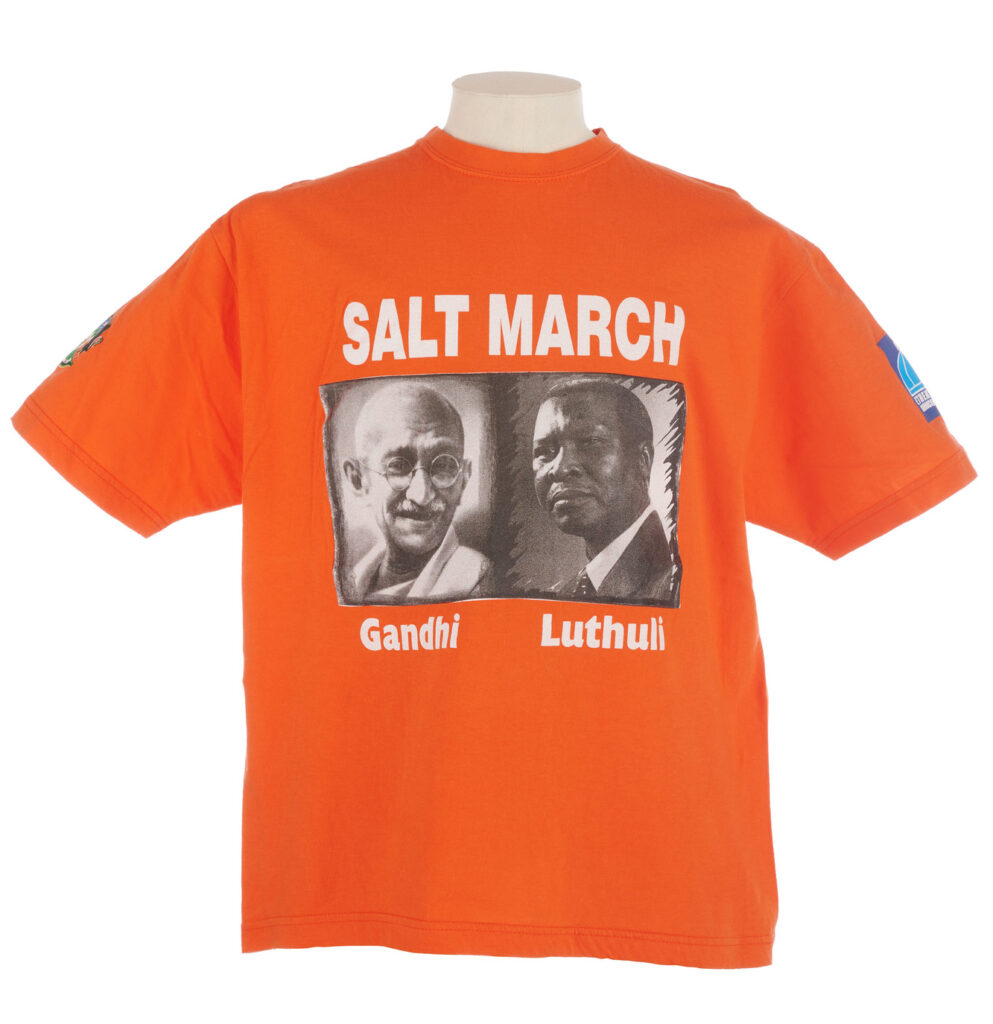 Orange Salt March T shirt with black and white portraits of Gandhi and Luthuli on the front