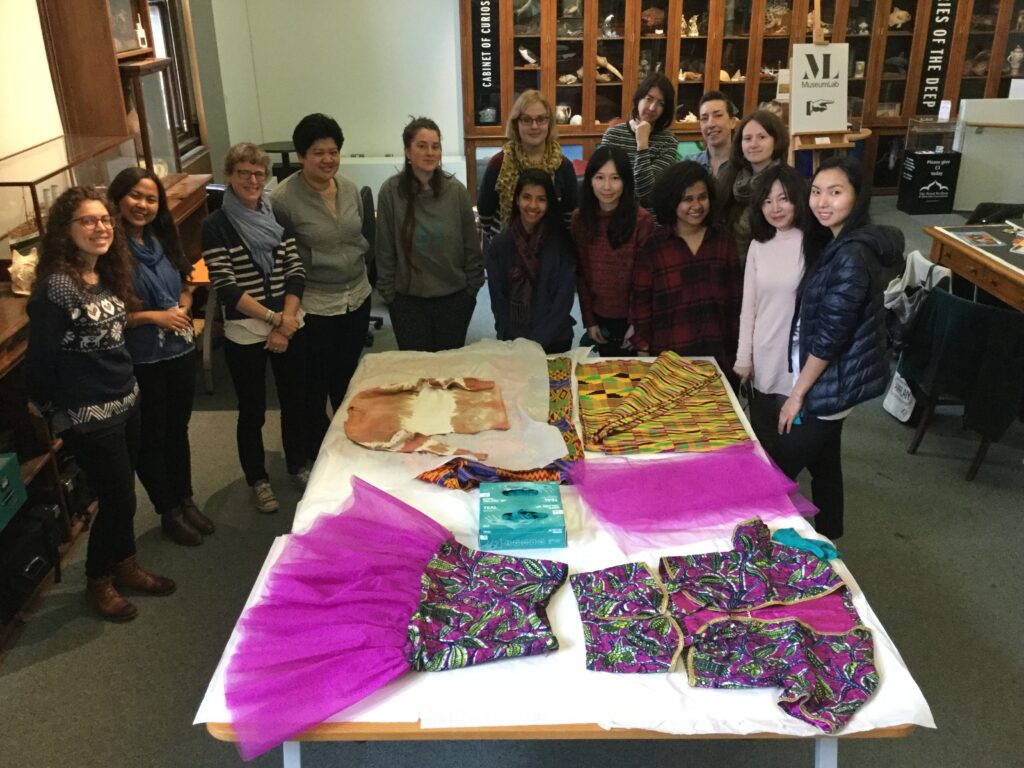 A group of students looking at textiles and garments laid out on a table.
