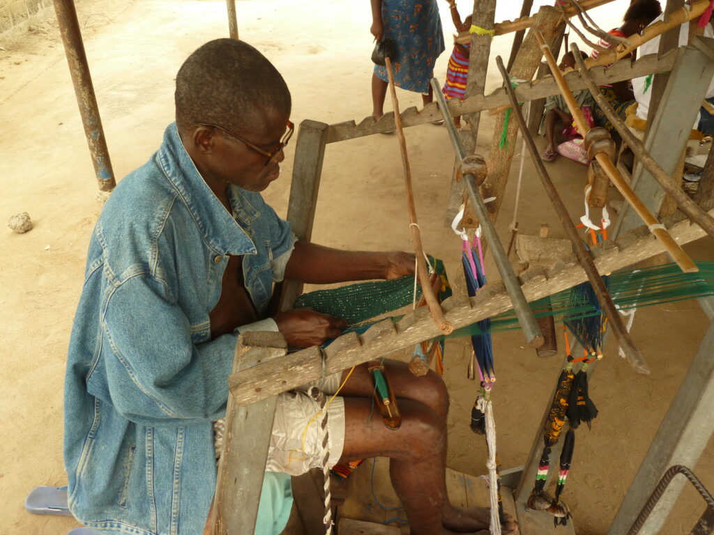 a man weaving a kente cloth at a large wooden loom