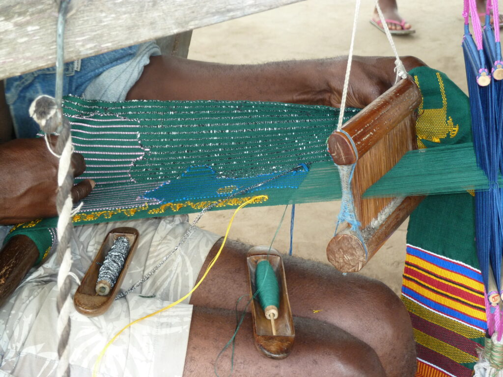 a man weaving a kente cloth with metallic green thread