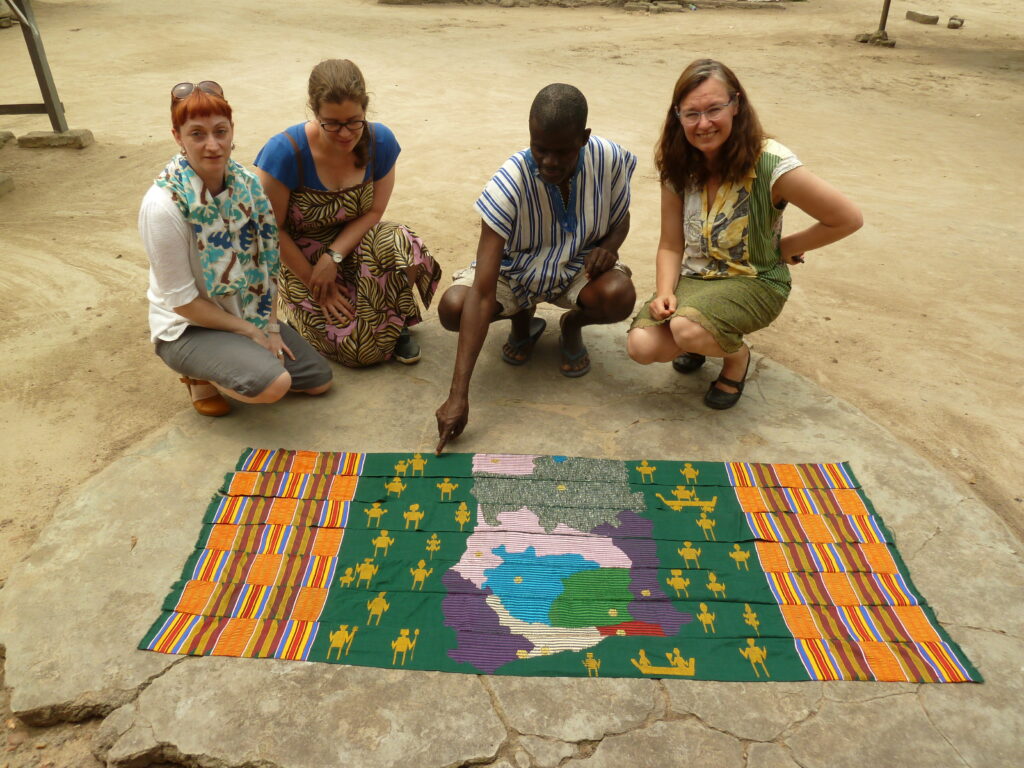 three women and a man crouch on the ground next to a kente cloth