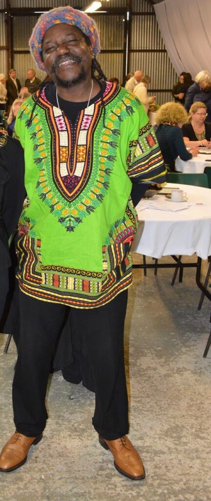 a man standing at an event wearing a green dashiki over black trousers